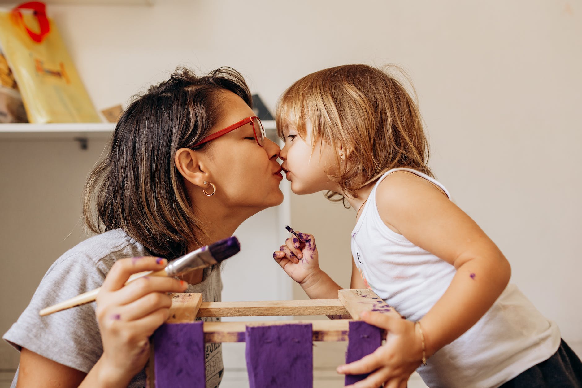 mother and daughter with paintbrushes in their hands kissing each other